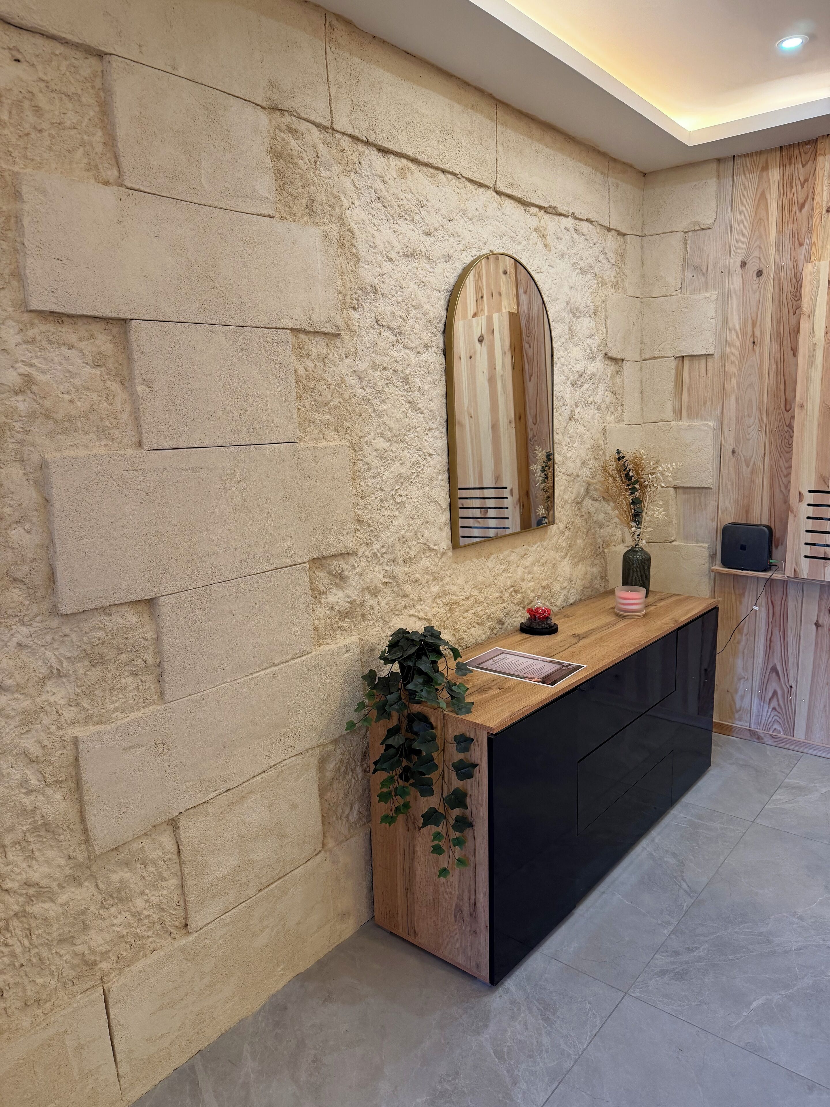 Un espace d’accueil avec un mur en pierre, un comptoir en bois, un miroir et une plante.