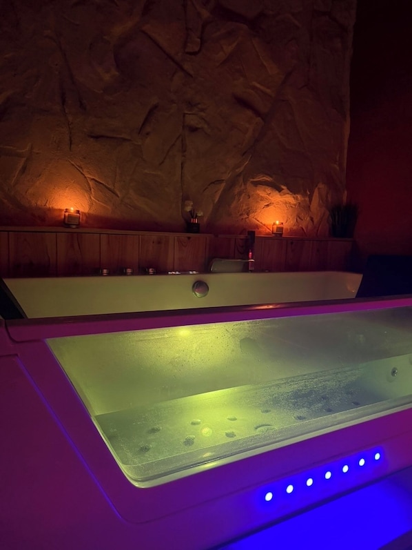 Um quarto de spa com uma banheira grande, armários de madeira e uma parede com superfície texturizada.