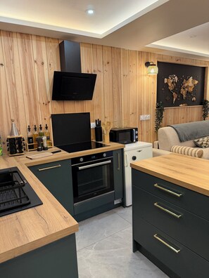 A modern kitchen with wooden cabinetry, a built-in oven, a microwave, and a black range hood. - Studio chaleureux, massage et bain (Cussac-Fort-Médoc)