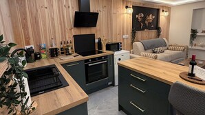 Una cucina moderna con pareti rivestite in legno, forno integrato e zona pranzo con divano grigio e un tavolino.