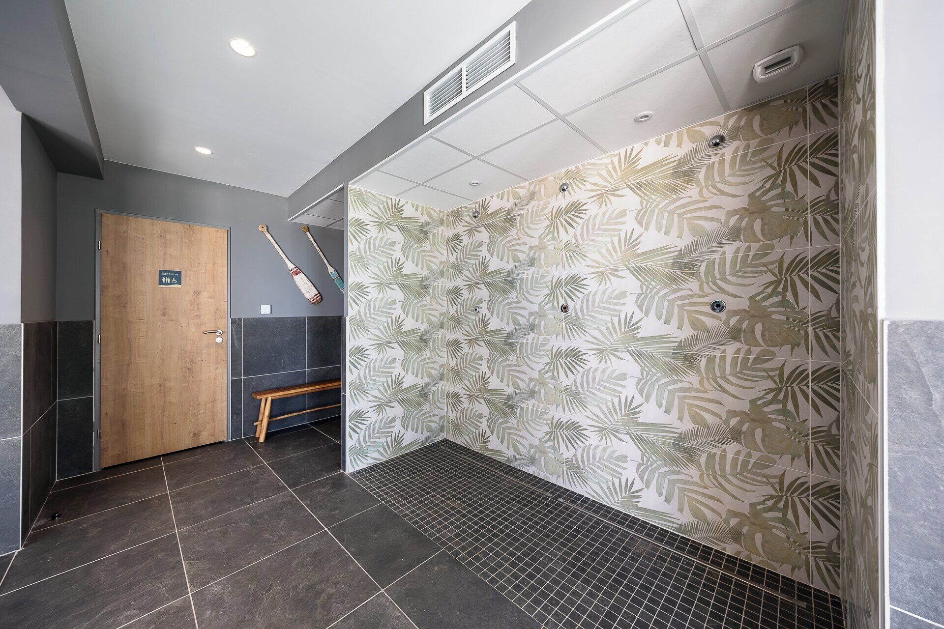 Un baño moderno con una puerta de madera, un banco y una pared con un diseño de hojas.