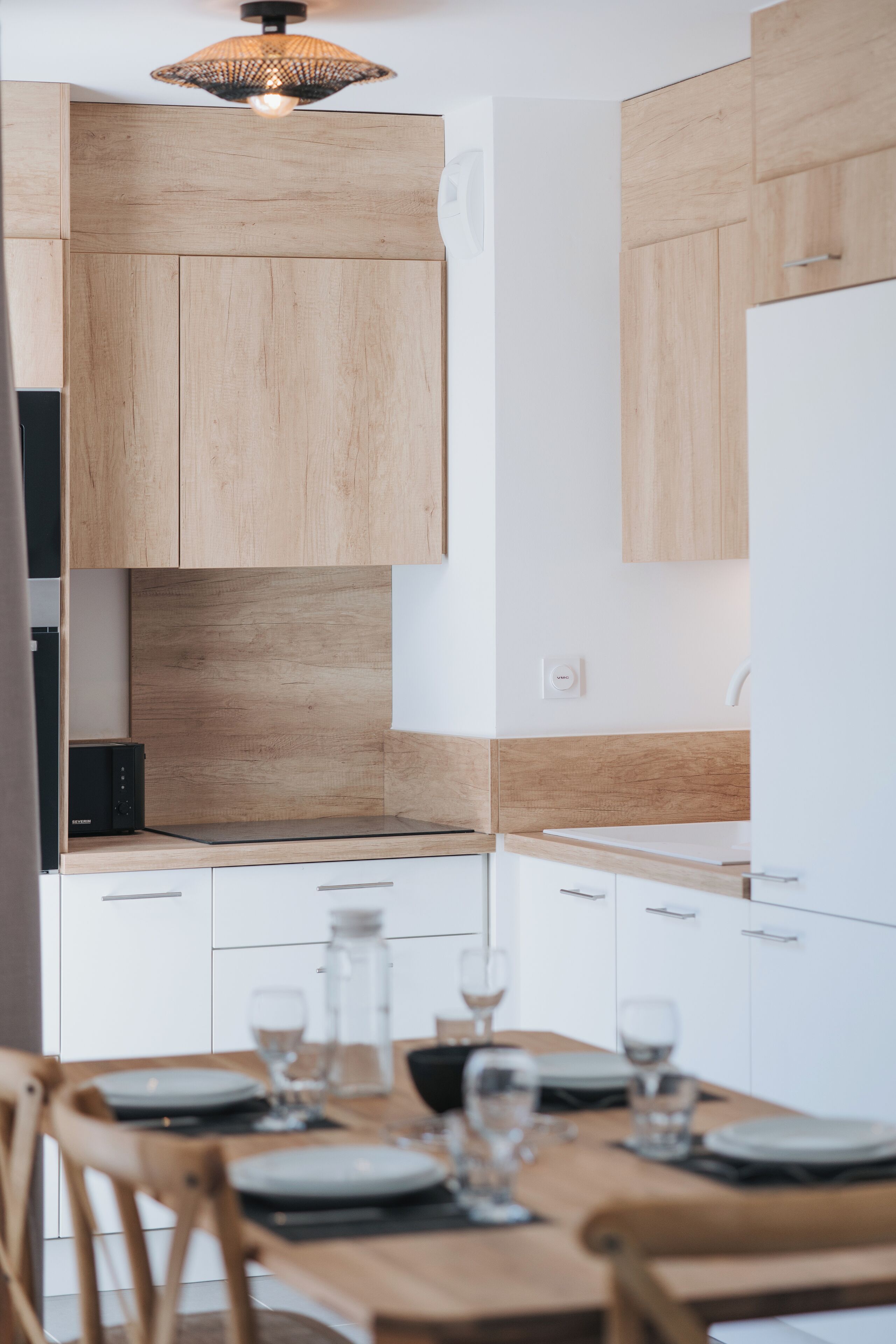 A modern kitchen with wooden cabinets, a built-in microwave, and a dining area with a table set for four.