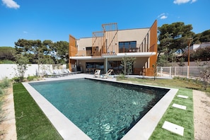 A modern two-story house with a swimming pool, a balcony with sun loungers, and a well-maintained lawn.