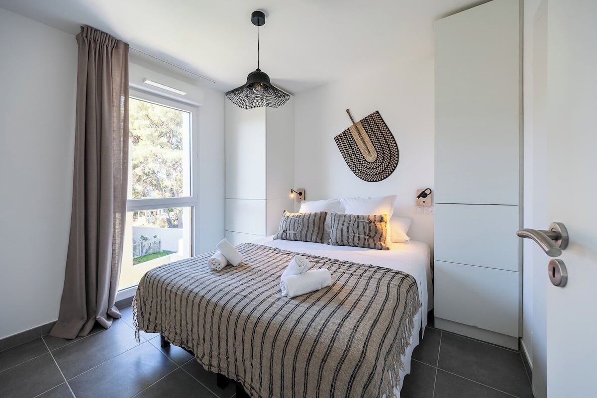 A modern bedroom with a large bed, a hanging light fixture, and a view of the outdoors.