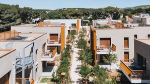 A modern residential complex with multiple apartment buildings, outdoor seating areas, and a central pathway. - La Corniche Bleue (Sausset-les-Pins)