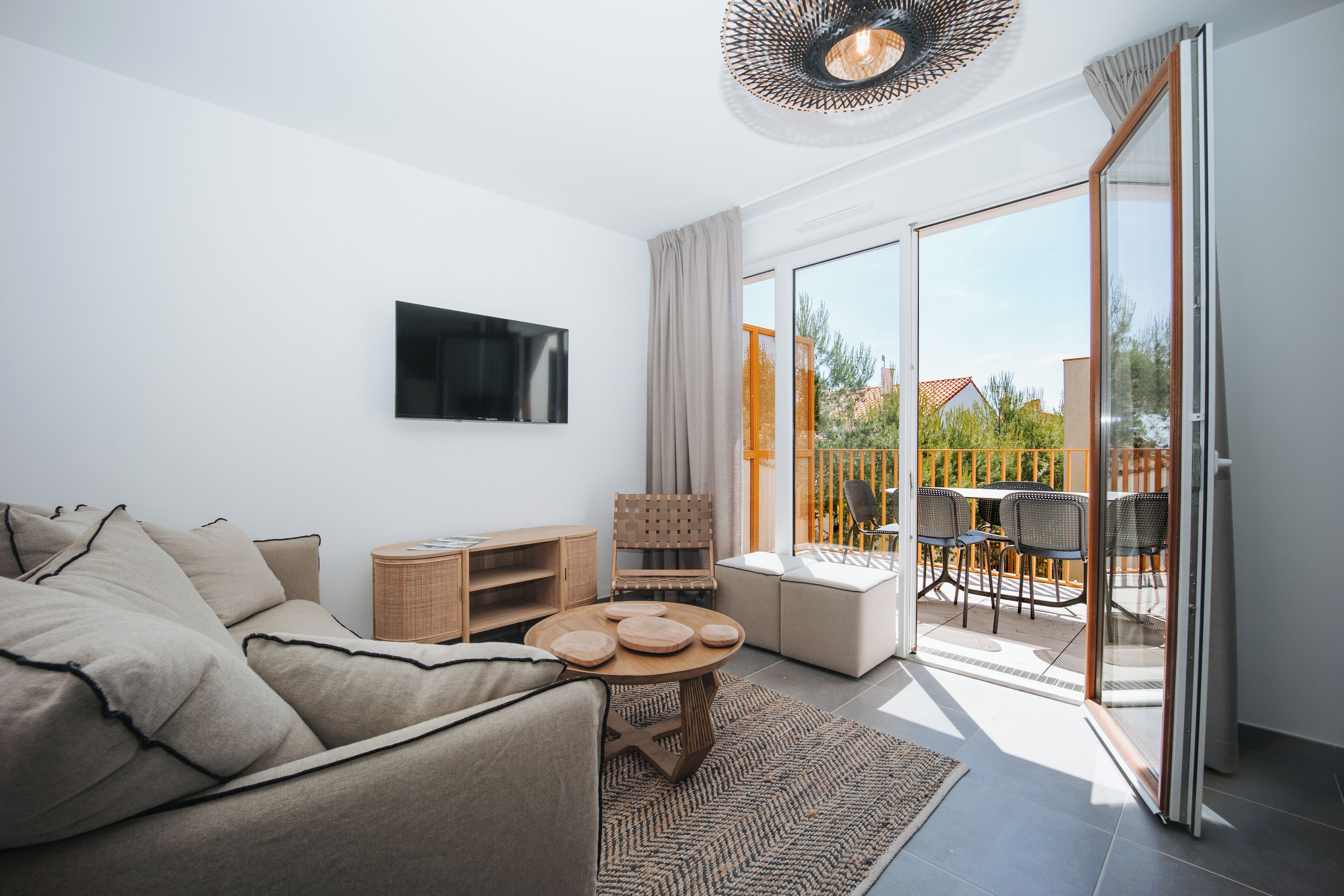 A modern living room with a sofa, a TV, a dining table with chairs, and a sliding glass door leading to an outdoor patio.
