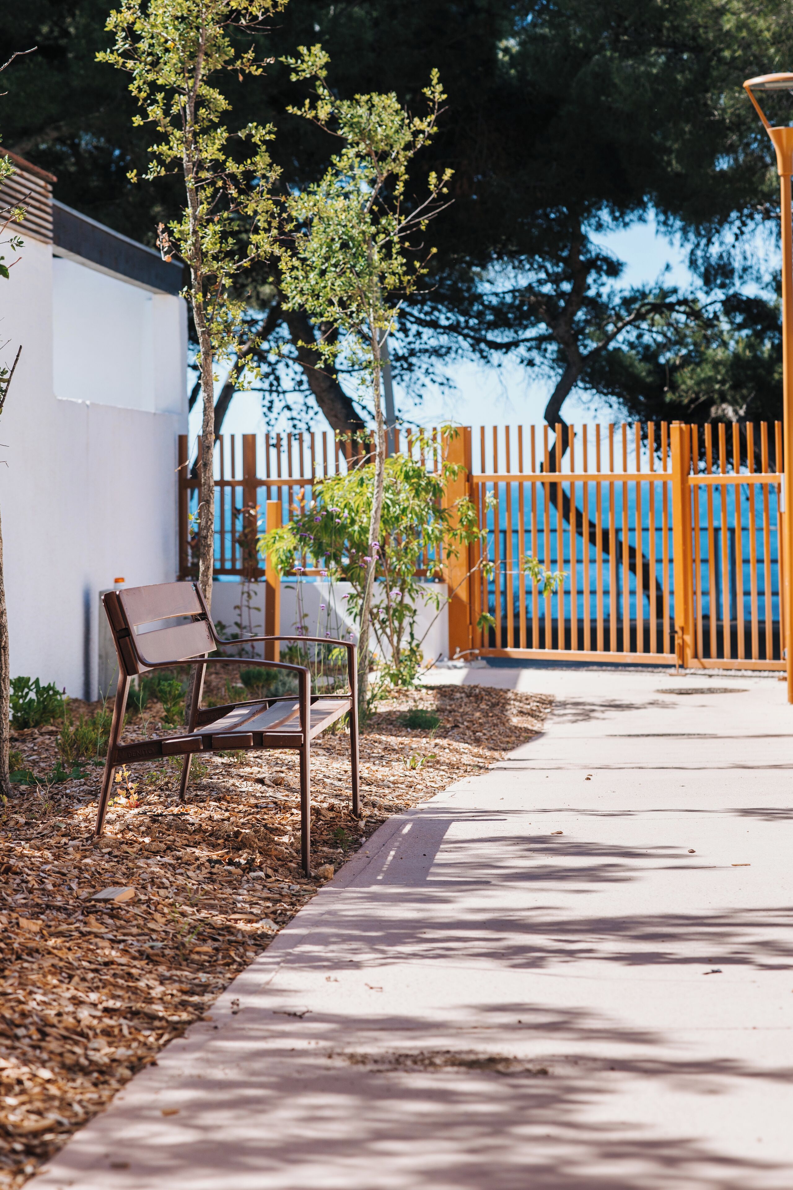 Un banc se trouve devant un bâtiment, avec une clôture et des arbres en arrière-plan.