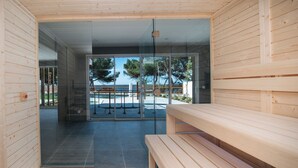 A modern sauna with wooden benches and glass doors leading to an outdoor area with a pool and trees. - La Corniche Bleue (Sausset-les-Pins)