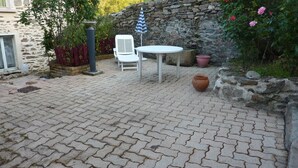 Eine gepflasterte Terrasse mit einem weißen Tisch und Stühlen, einer Steinmauer und Kübelpflanzen.