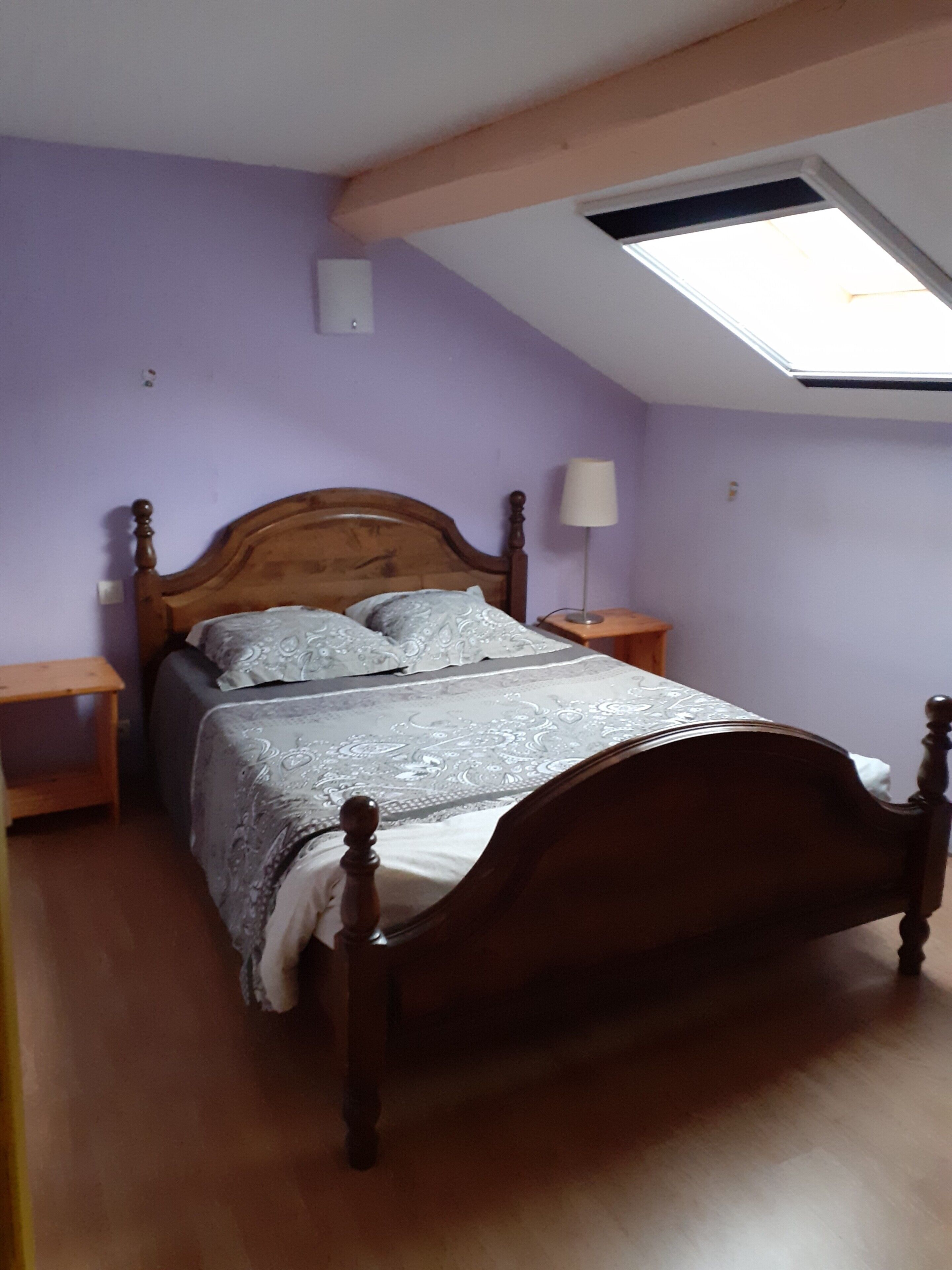 A bedroom with a wooden bed, a skylight, and purple walls.