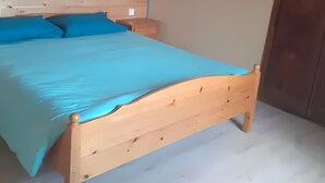 Ein Bett mit Holzbalken und einem blauen Überwurf in einem Zimmer mit Holzboden und einer schlichten Wand.