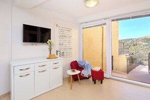 Moderni olohuone, jossa on televisio, seinä täynnä inspiroivia sitaatteja, punainen sohva, pieni pöytä, jonka päällä on kirja, ja parveke, josta on kaunis näköala.