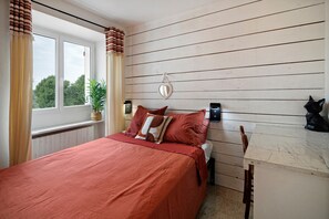 Een slaapkamer met een bed, nachtkastje, een plant in pot, een spiegel en een kat.