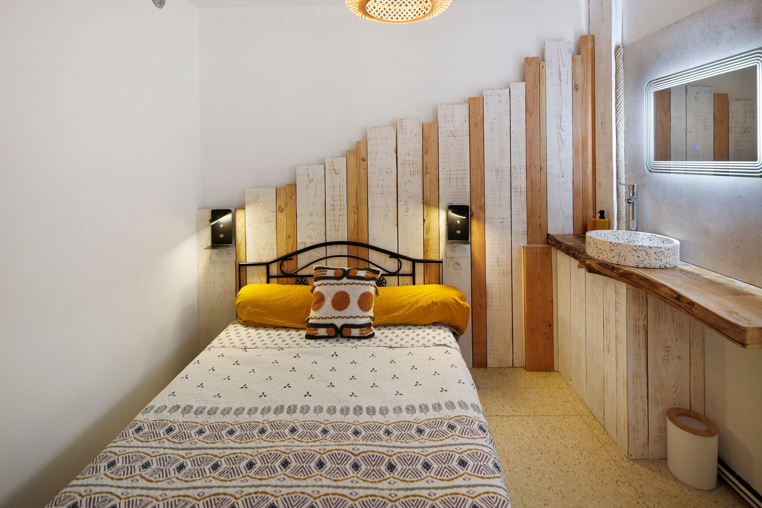 Ein Schlafzimmer mit einem Bett, einem Nachttisch, einem Spiegel und einer Wandleuchte.
