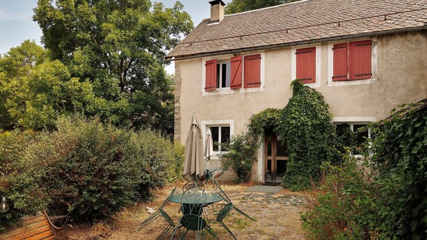 Een huis met een pannendak, rode luiken en een tuin met een tafel en stoelen.