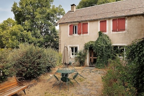 A house with a tiled roof, red shutters, and a garden with a table and chairs.