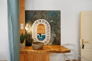 Un banco de madera con un cuenco de piedra, una planta en maceta y un espejo con marco decorativo colgado en la pared.