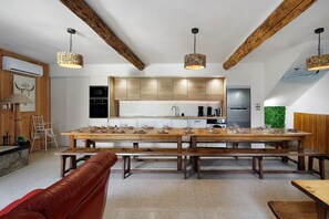 Una cocina moderna con vigas de madera, una mesa larga para seis comensales y luces colgantes.