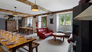 Een ruime woonkamer met een houten eettafel, gedekt voor een maaltijd, een rode leren bank en een open haard.