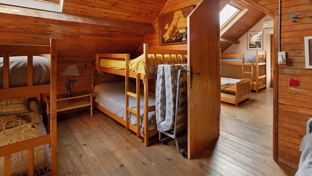 Ein gemütliches Blockhaus mit Holzwänden und -böden, Etagenbetten, einem kleinen Tisch mit Lampe und einem Bild an der Wand.