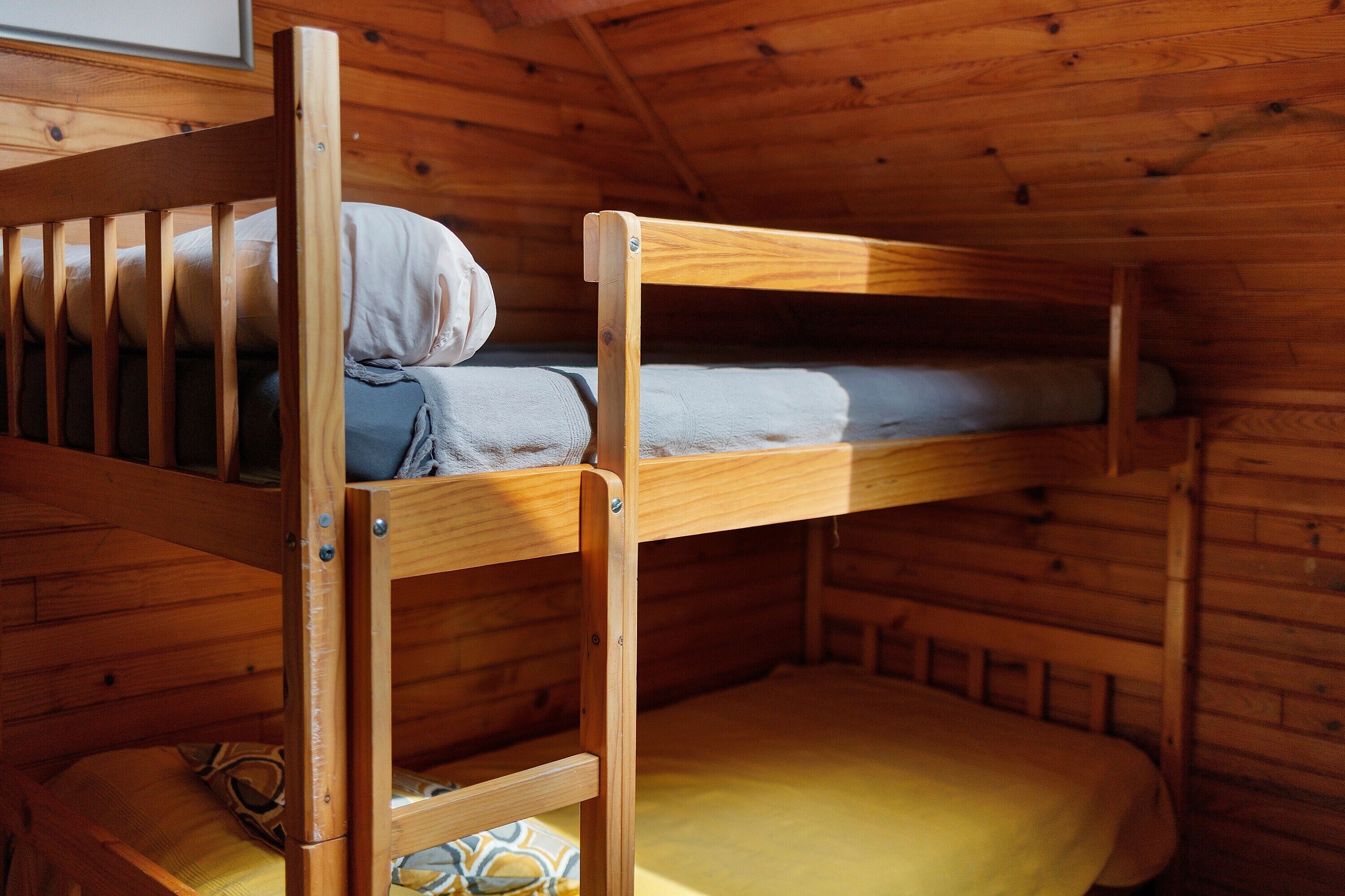 Ein Stockbett mit Holzrahmen und einer unteren Liege mit gelber Matratze.