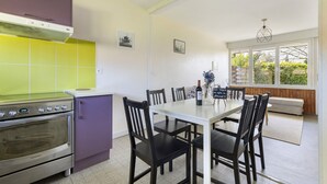 A kitchen with a stove, dining table, chairs, and a window with a view of greenery. - Mirabel Cottage at Château Saint Ahon (Blanquefort)