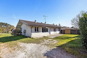 Une maison de plain-pied avec un toit en pente, un porche à l’avant et un petit jardin devant, avec un chemin de gravier.