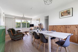 Un comedor moderno con una mesa blanca, sillas negras y un sillón antiguo.