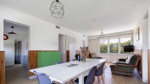 Una cocina moderna con encimera blanca, armarios de madera y una zona de comedor con mesa y sillas blancas.