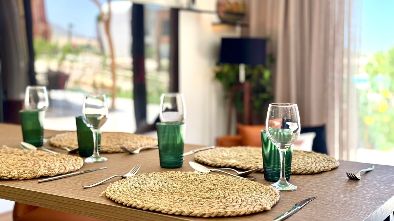 A dining table set with green glassware and woven placemats.