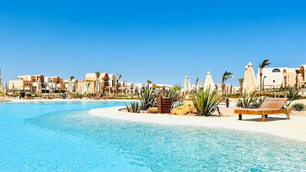 Un espace piscine aménagé dans un complexe hôtelier, avec une eau d’un bleu limpide, des palmiers et des chaises longues.