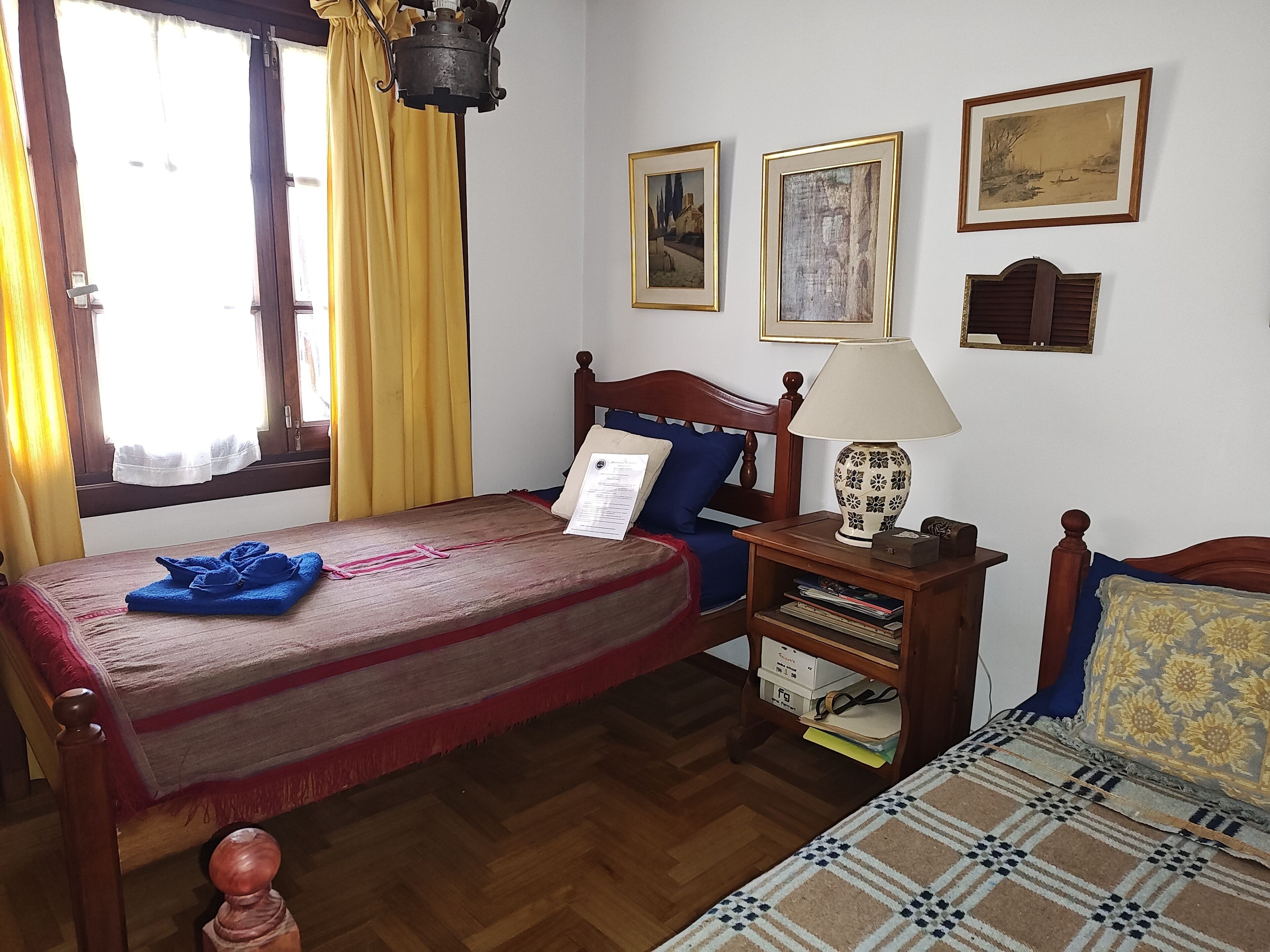 A room with a wooden bed, a nightstand with a lamp, and two framed pictures on the wall.