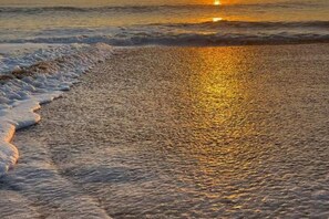 Ein Strand mit sanft anschwellenden Wellen und einem Sonnenuntergang im Hintergrund.
