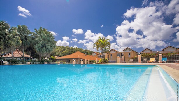 Una piscina con agua azul cristalina, rodeada de palmeras y edificios con tejados rojos.