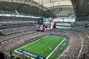 A large indoor stadium with multiple tiers of seating, a central field, and large digital displays. - Walk to AT&T Stadium, 3 King Beds, Lux 2BR, Free Parking, 2 Gig WiFi (Arlington)
