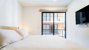 Ein Hotelzimmer mit einem großen Bett, einem an der Wand befestigten Fernseher und einem Balkon mit Blick auf das Gebäude.