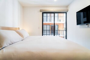 Une chambre d’hôtel avec un grand lit, un téléviseur fixé au mur et un balcon offrant une vue sur l’immeuble.