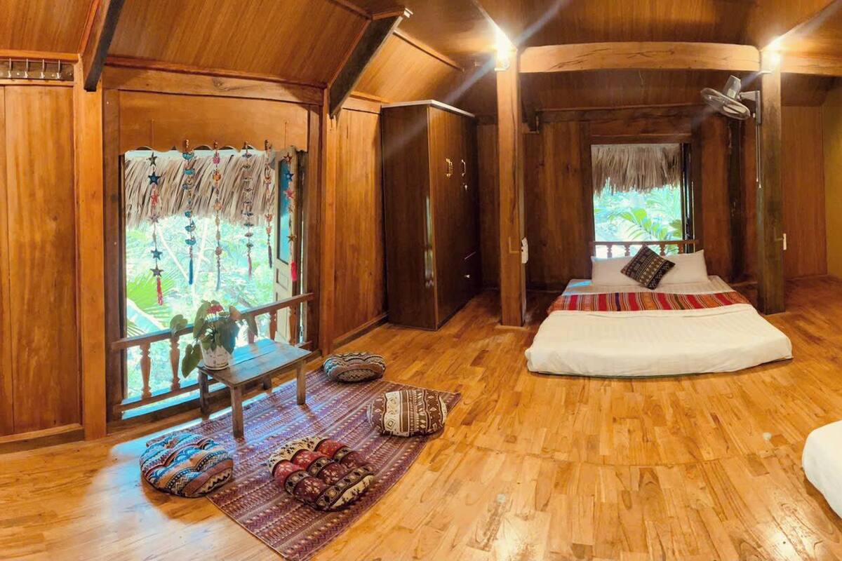 Une pièce en bois avec un lit, un banc et une vue sur la verdure à l’extérieur.