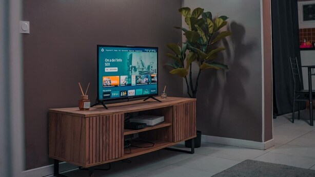 Una sala de estar con un televisor sobre un mueble de madera, un reloj en la pared y un cuadro enmarcado.