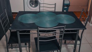 Comedor con una mesa dispuesta para cuatro personas, rodeada de sillas de metal. Se ve una lavadora al fondo.