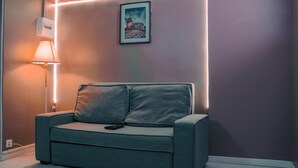 Una sala de estar moderna con un sofá gris, un cuadro del Coliseo y una lámpara de pared.