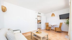 Una sala de estar moderna con un sofá, una mesa de centro, sillas de mimbre, un televisor y una cocina al fondo.