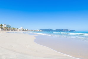 Une plage avec un ciel dégagé, un rivage sablonneux et des bâtiments en arrière-plan.