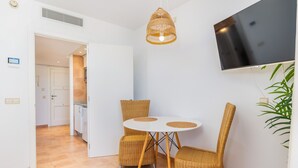 Una habitación con un televisor en la pared, sillas de mimbre alrededor de una mesita y una puerta que da a otra estancia.