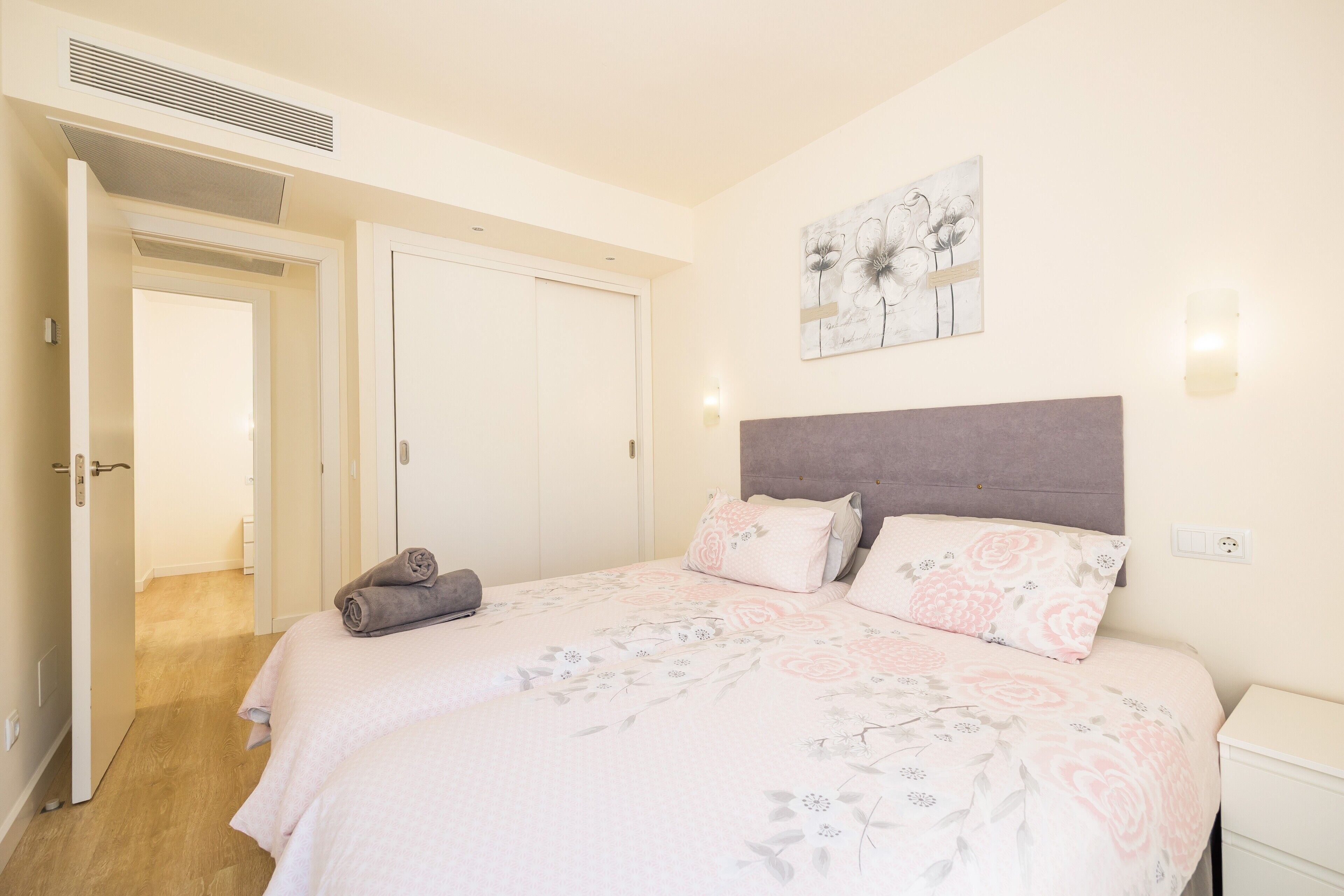 A bedroom with a bed, a nightstand, a wall-mounted light, and a door leading to another room.