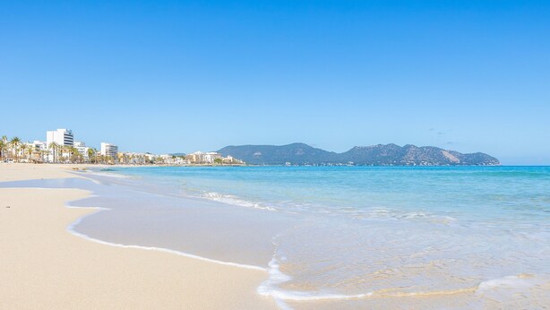 A beach with clear water, a sandy shore, and buildings in the background. - Incredible Sea Views – 50 m from Cala Millor Beach (Cala Millor)