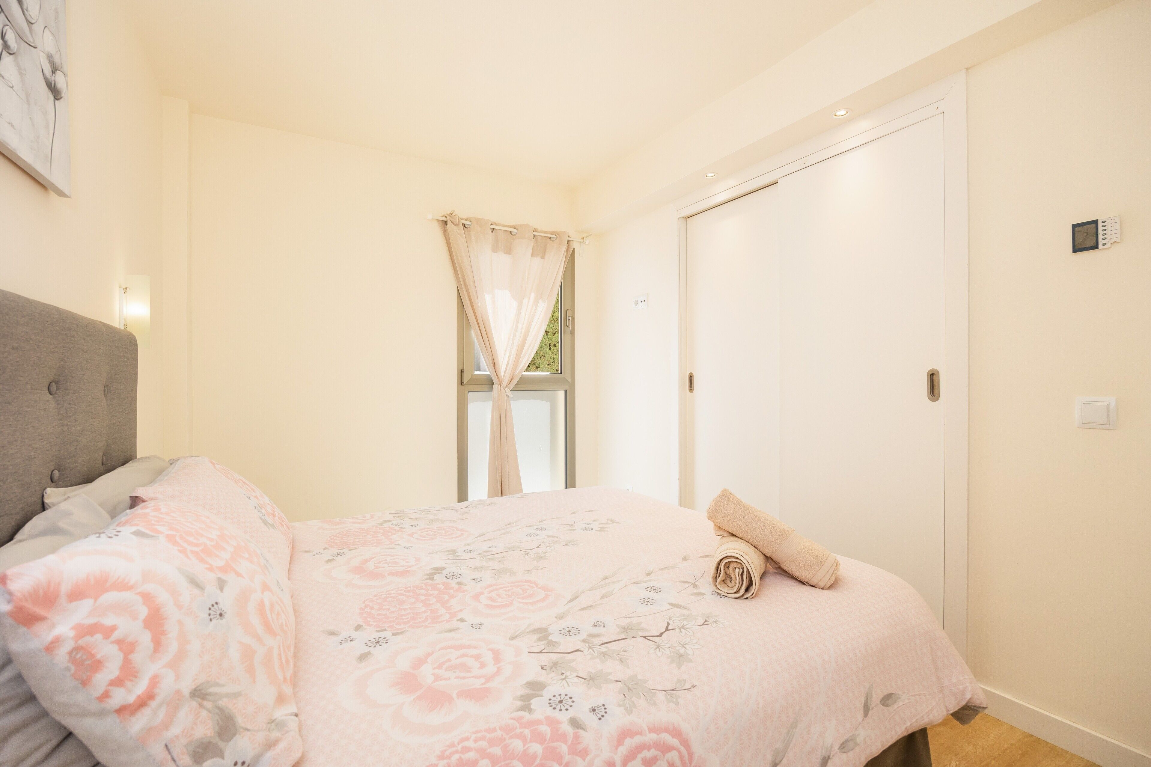 A bedroom with a bed, a window with curtains, a door, and a wall-mounted light.