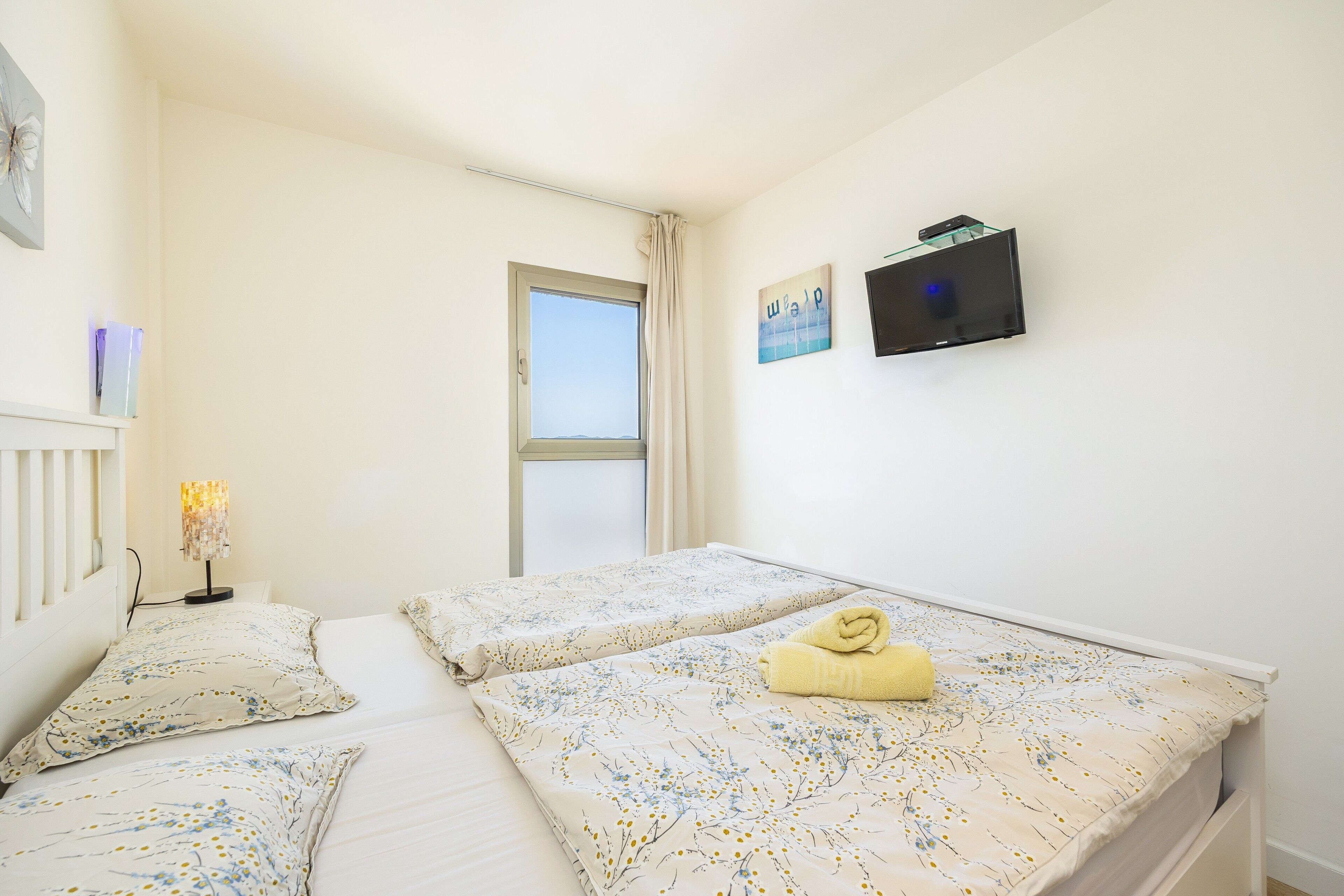 Ein Zimmer mit zwei Betten, einem Fenster, einem Fernseher und einer Lampe.