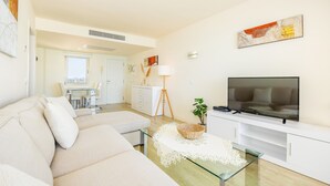 Un soggiorno moderno con un divano, televisione e un'area pranzo sullo sfondo.