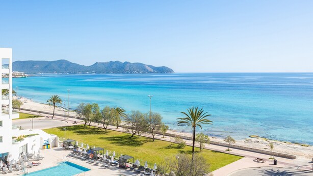 Un hotel sulla costa con piscina, lettini e vista sul mare e sulle montagne.